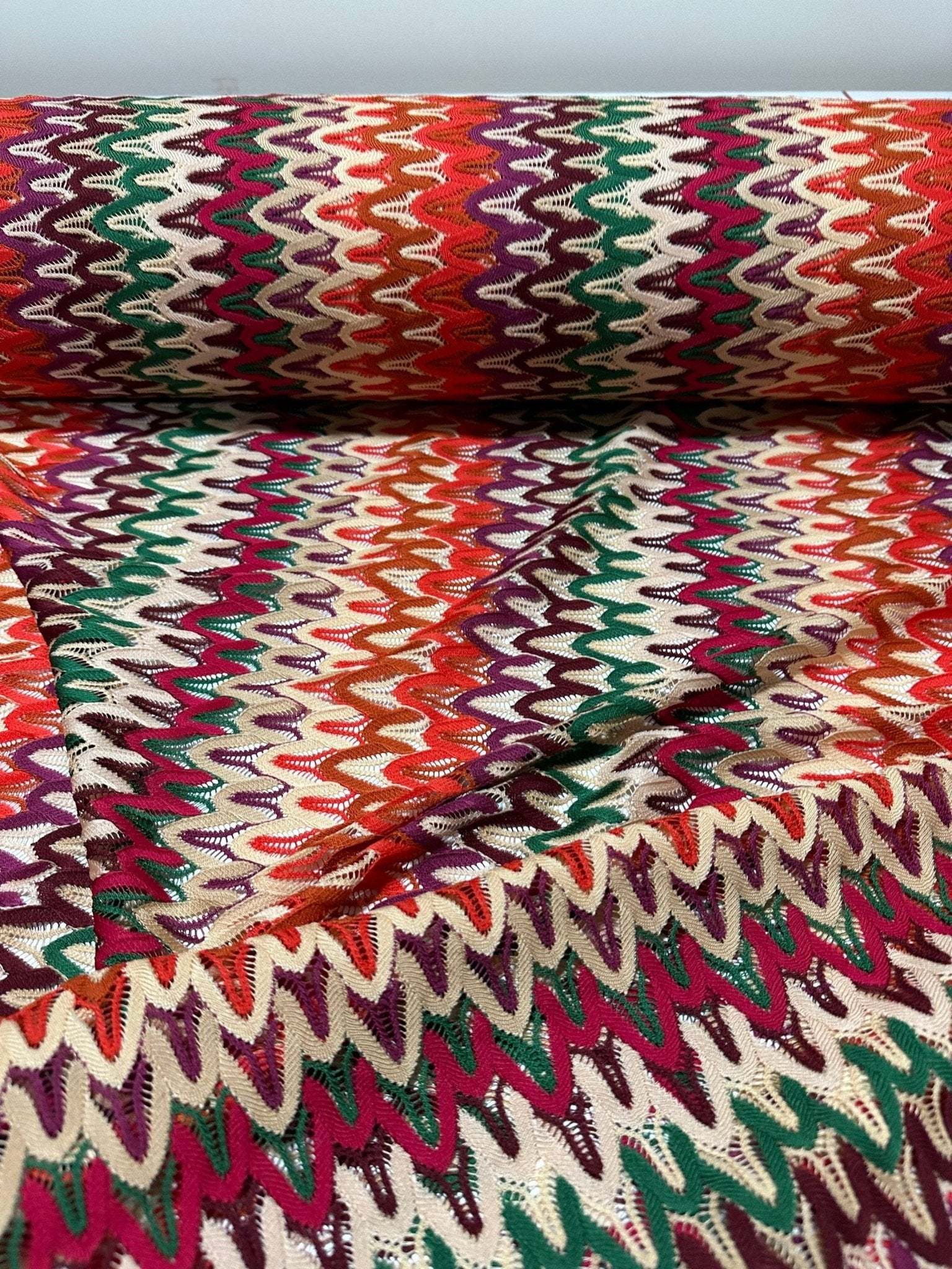 Multicolor zigzag knit jersey fabric with chevron pattern in vibrant red, green, purple, and cream tones, perfect for clothing projects.