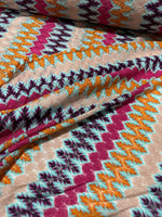 Close-up of colorful zigzag knit jersey fabric with multicolor chevron pattern in purple, orange, teal, and beige tones