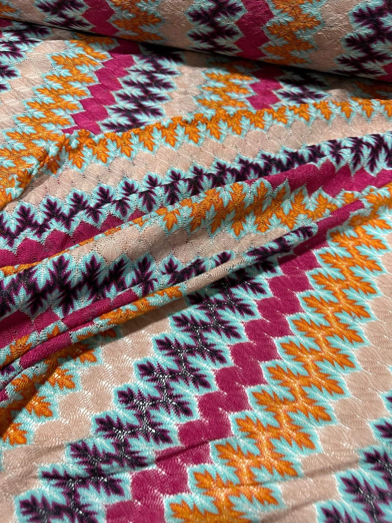 Close-up of colorful zigzag knit jersey fabric with multicolor chevron pattern in purple, orange, teal, and beige tones