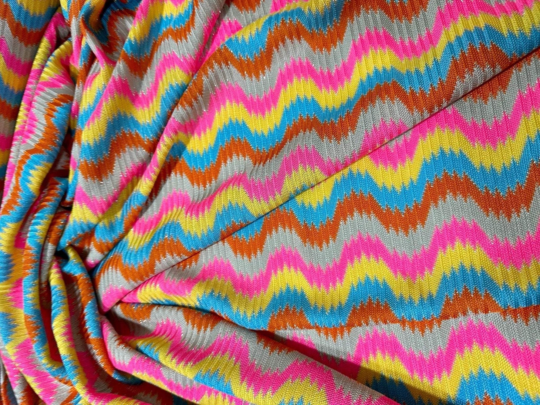 Luxury zigzag knit jersey fabric with pink, blue, yellow, and orange chevron pattern, soft and stretchy.