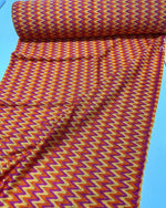 Chevron zigzag knit jersey fabric in orange, yellow, and purple rolled out on blue background