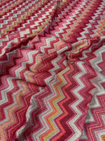 Zigzag Lurex Knit Fabric in shimmering gold with vibrant pink, red, and yellow zigzag patterns on polyester knit material.