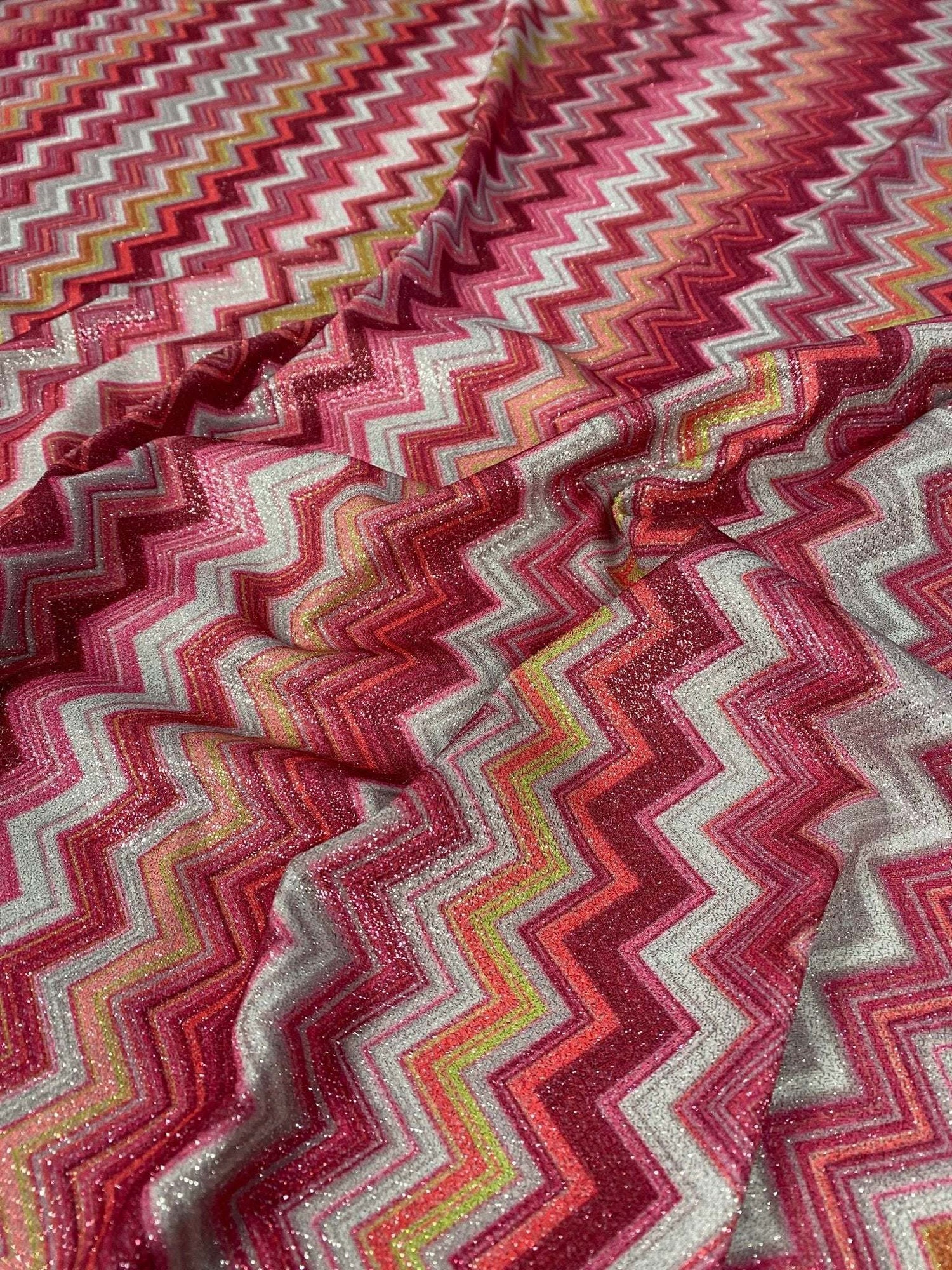 Zigzag Lurex Knit Fabric in shimmering gold with vibrant pink, red, and yellow zigzag patterns on polyester knit material.