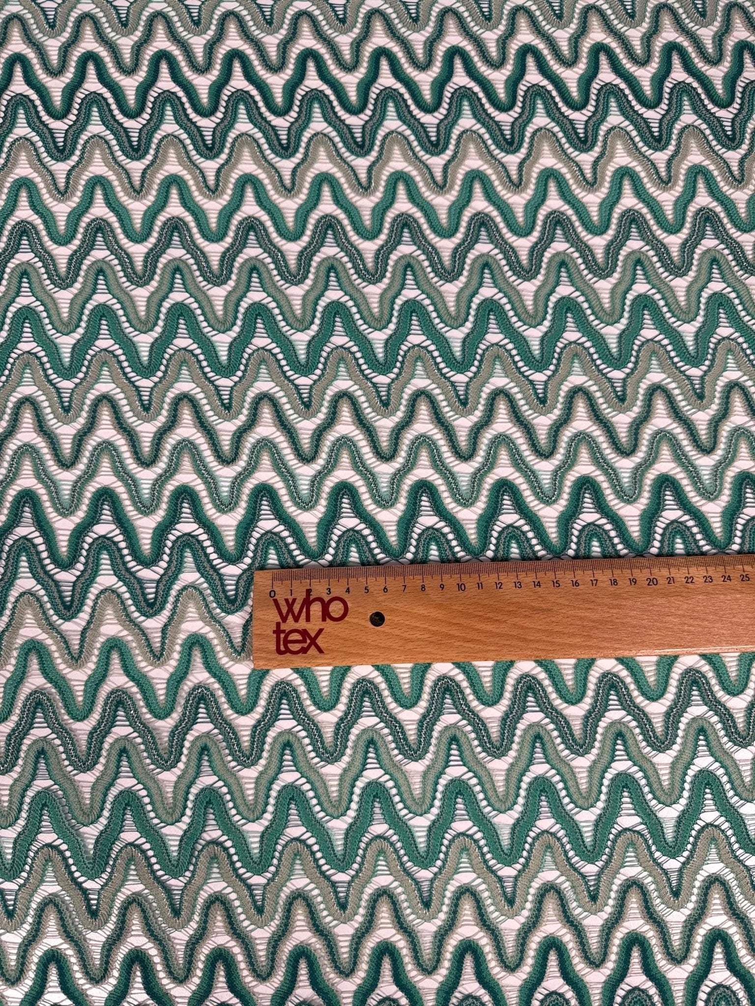 Zigzag mesh fabric in green tones with rhythmic knit pattern and ruler for scale