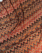 Close-up of Zigzag Shimmer Fabric in orange and black with 4-way stretch and glittering Lurex threads