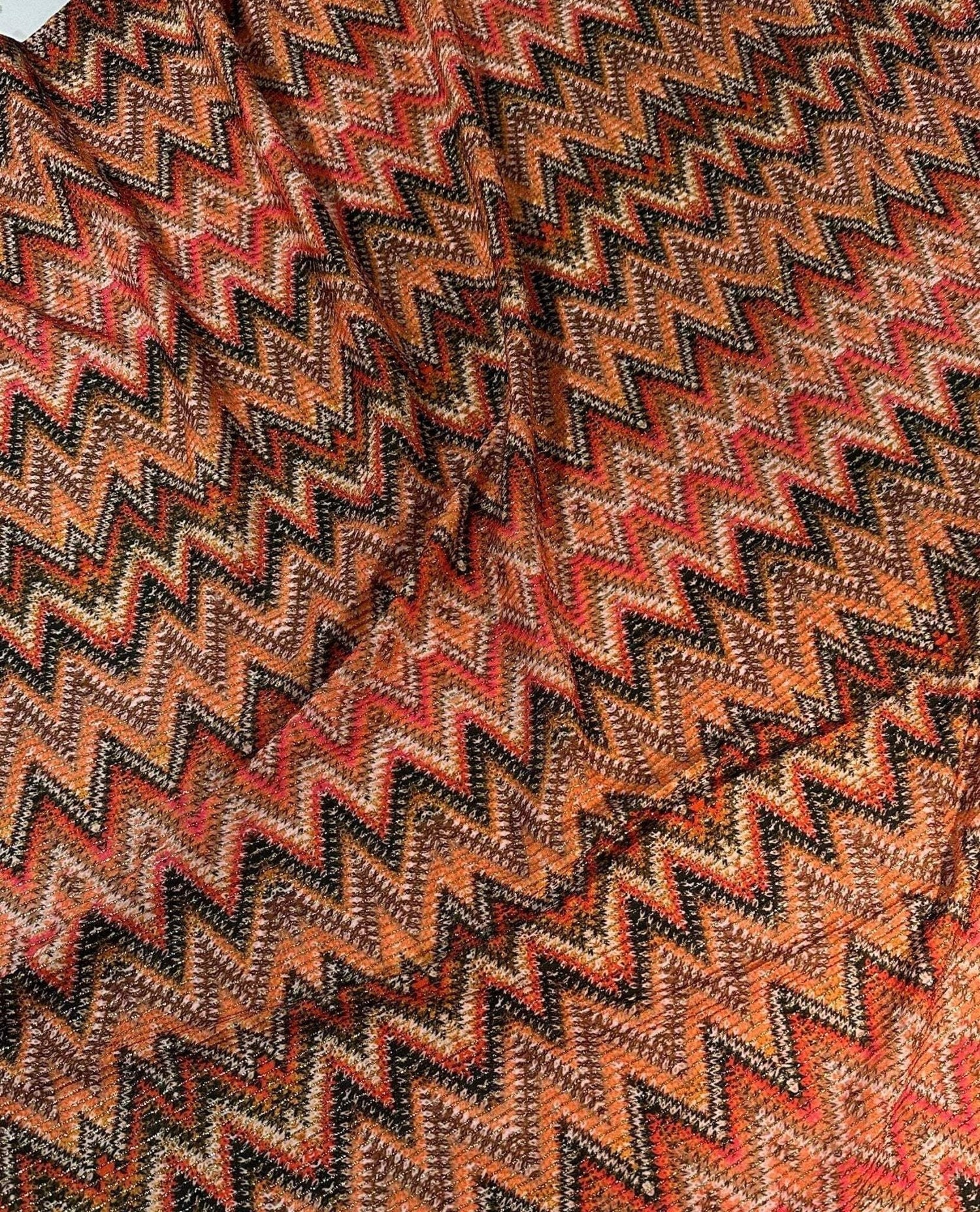 Close-up of Zigzag Shimmer Fabric in orange and black with 4-way stretch and glittering Lurex threads